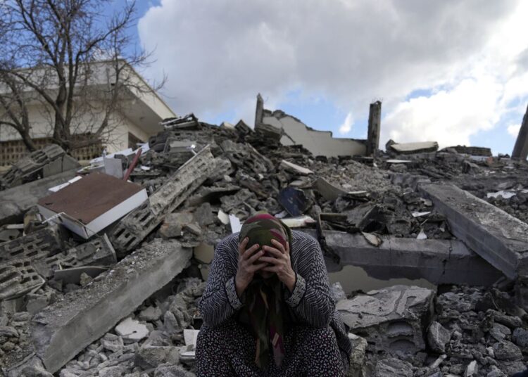 A woman sits on the rubble as emergency rescue teams search for people under the remains of destroyed buildings in Nurdagi town on the outskirts of Osmaniye city southern Turkey, Feb. 7, 2023.