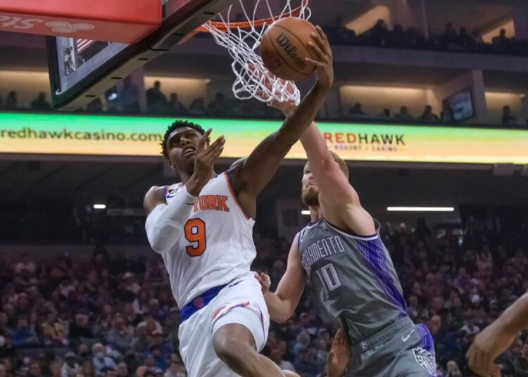 New York Knicks RJ Barrett (L) lays the ball up past Sacramento Kings Domantas Sabonis during an NBA game in Sacramento, Calif.