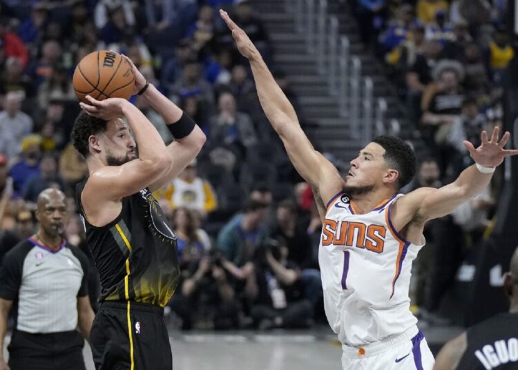 Golden State Warriors guard Klay Thompson (L) makes a 3-point basket against Phoenix Suns guard Devin Booker during an NBA basketball game in San Francisco.