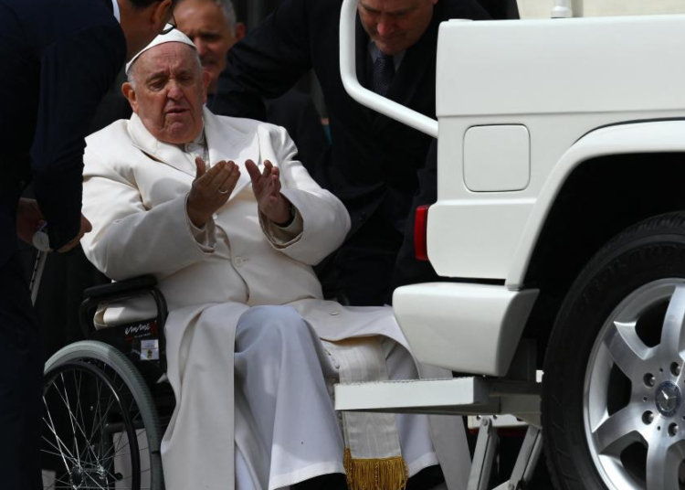 Pope Francis speaks with his aides prior to being helped get up the popemobile car from his wheelchair, as he leaves on March 29, 2023 at the end of the weekly general audience at St. Peter's square in The Vatican. AFP
