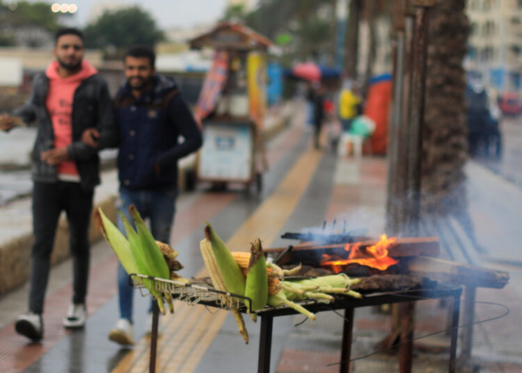 FILE PHOTO: People walk next to a corn seller during rainy weather in the Mediterranean port city of Alexandria, Egypt December 31, 2021. REUTERS/Amr Abdallah Dalsh
