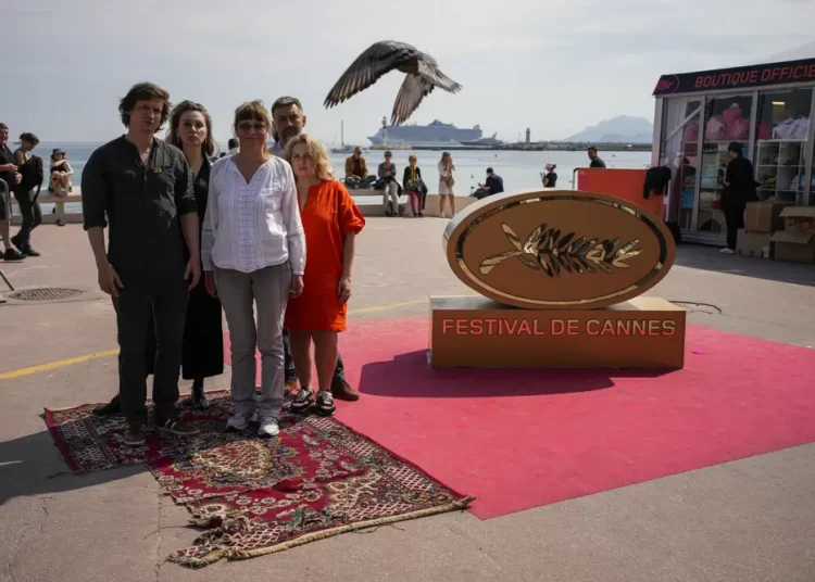 The crew of the documentary 'In the Rearview', Maciek Hamela, from left, Kseniia Marchenko, Larysa Sosnovtseva, Yura Dunay, and Anna Palenchuk standing on a rug damaged by a bomb in the town of Lukashivka in Ukraine on the Boulevard de la Croisette during the 76th edition of the Cannes Film Festival in Cannes, southern France, on Sunday, May 21, 2023.