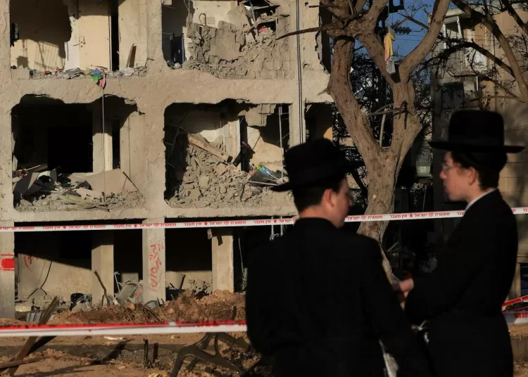People stand at the scene of damage after Iranian missile barrages struck residential buildings in Arad, amid the US-Israel conflict with Iran, in southern Israel, 22 March, 2026. Reuters