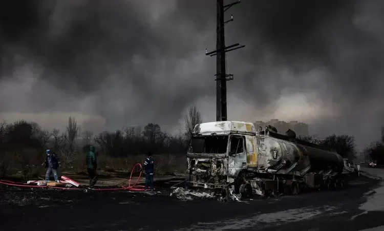 People stand near a destroyed vehicle as smoke rises after a reported strike on Shahran fuel tanks in Tehran, Iran, March 8, 2026. REUTERS