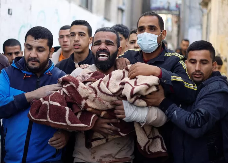 A Palestinian man reacts as he carries a casualty at the site of Israeli strikes on houses in Rafah, amid the ongoing conflict between Israel and the Palestinian Islamist group Hamas, in Rafah in the southern Gaza Strip, December 7, 2023.