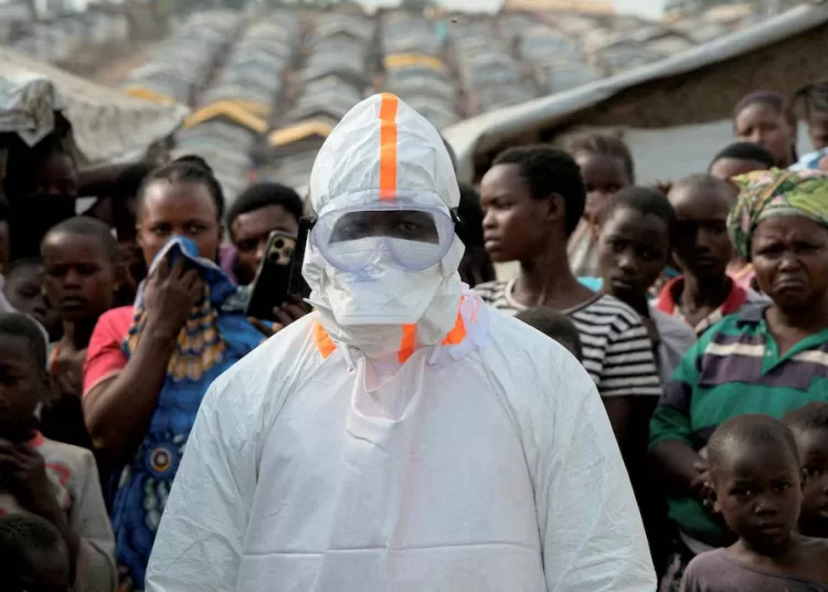 WHO faces Ebola funding shortfall 11 - Egyptian Gazette A health worker in personal protective equipment stands near displaced people waiting for the burial of suspected Ebola victims at the Kigonze displaced persons camp, one month after an outbreak was declared, in Bunia, eastern Democratic Republic of Congo, June 18, 2026.