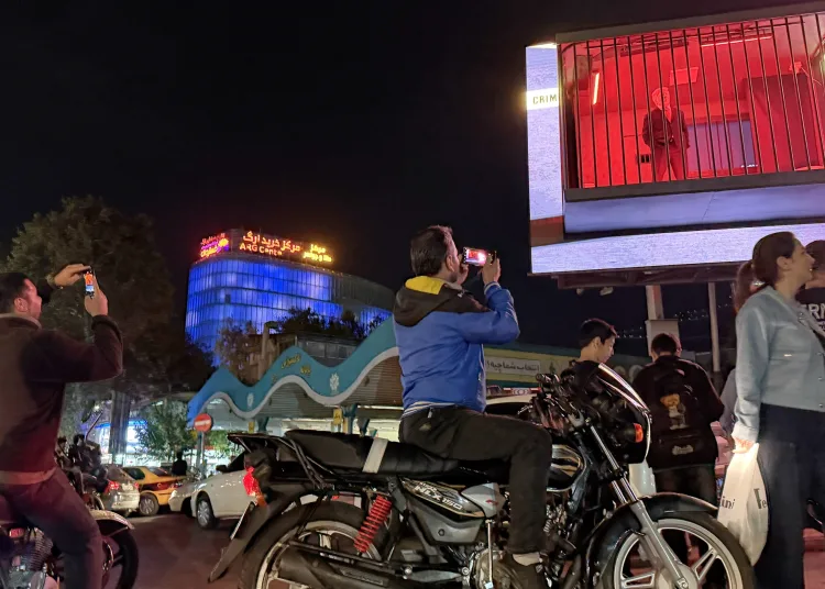 People take pictures of a billboard installation featuring an actor portraying President Donald Trump behind bars in a mock prison cell in Tajrish Square in Tehran.